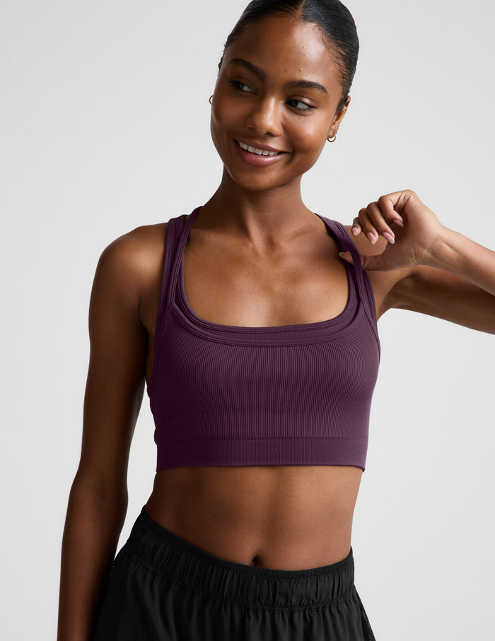 Woman wearing a purple sports bra and black shorts on a plain background.