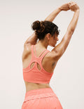 Woman in a coral sports bra and shorts stretching against a light background.
