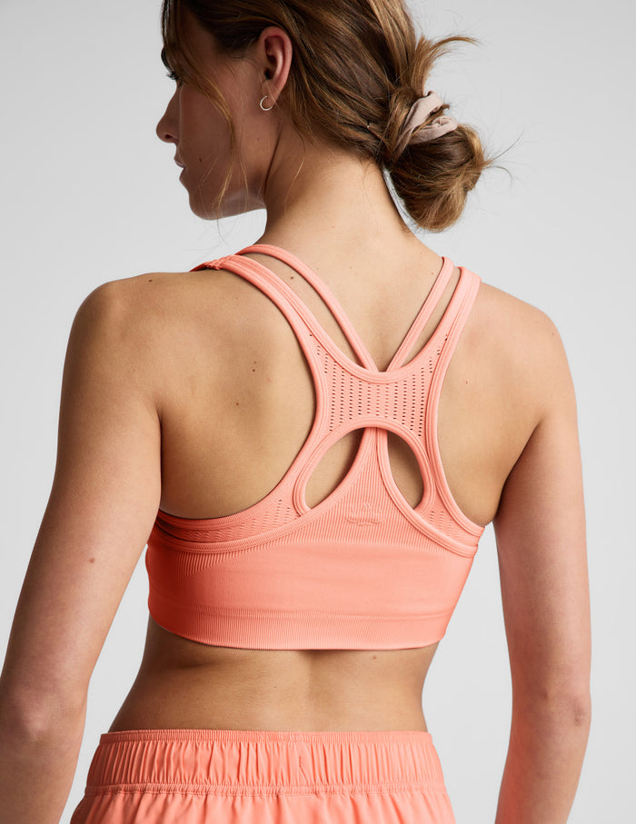 Woman wearing a coral sports bra and shorts on a light gray background.