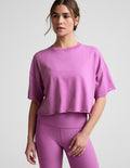Woman wearing a purple cropped t-shirt and leggings against a plain background.
