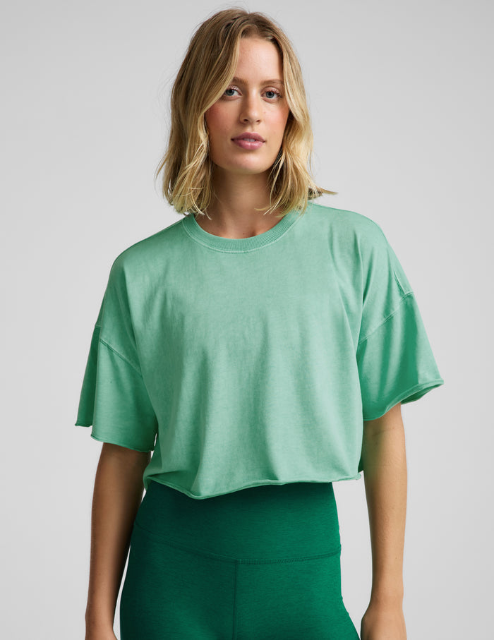 Woman wearing a light green cropped t-shirt and green biker shorts against a plain background.