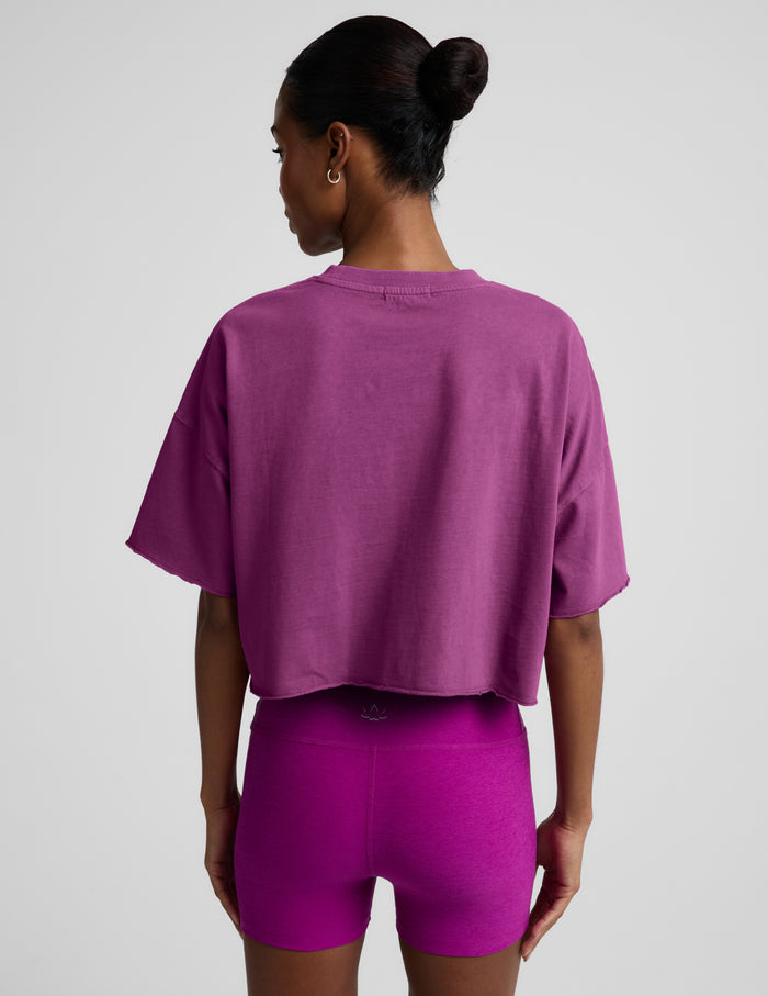 Woman wearing a purple cropped t-shirt and purple biker shorts against a plain background.