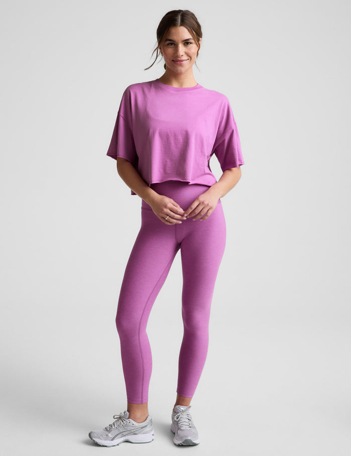 Woman wearing a purple cropped t-shirt and leggings against a plain background.