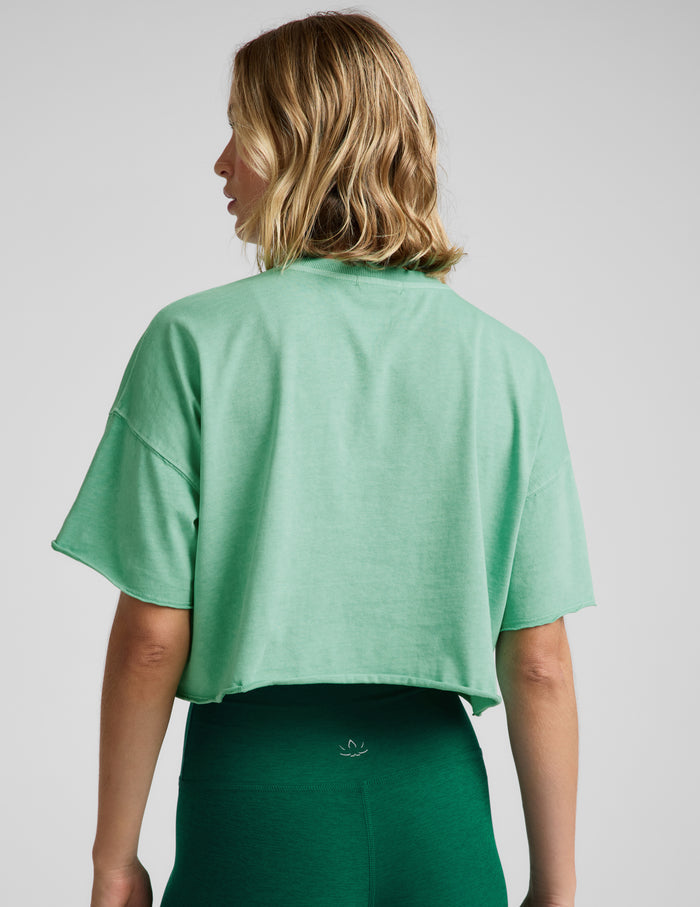 Woman wearing a light green cropped t-shirt and green biker shorts against a plain background.
