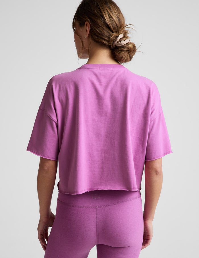 Woman wearing a purple cropped t-shirt and leggings against a plain background.
