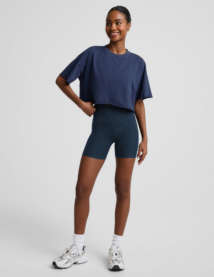 Woman wearing a navy blue cropped t-shirt and navy biker shorts against a plain background.