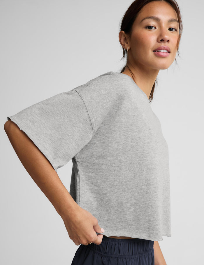 A woman modeling a light gray cropped short-sleeve t-shirt and navy blue athletic shorts against a light gray studio background.