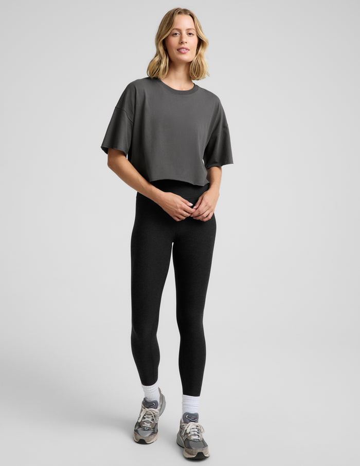 Woman wearing a dark gray cropped t-shirt and black leggings against a plain background.