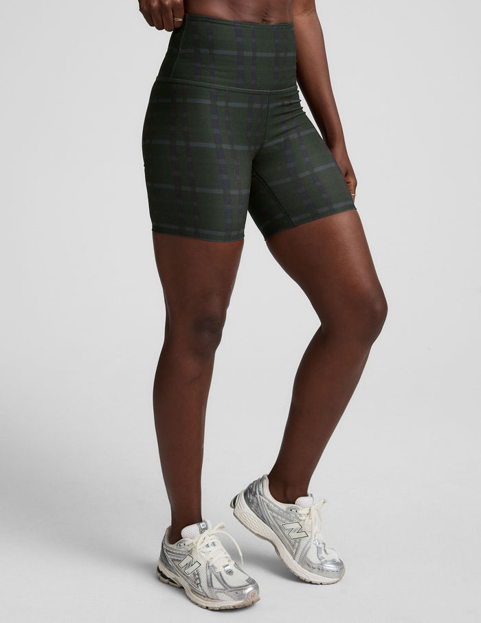 Emerald plaid SoftMark Keep Pace Biker Short with a high waistband and 5-inch inseam on a model with white sneakers.