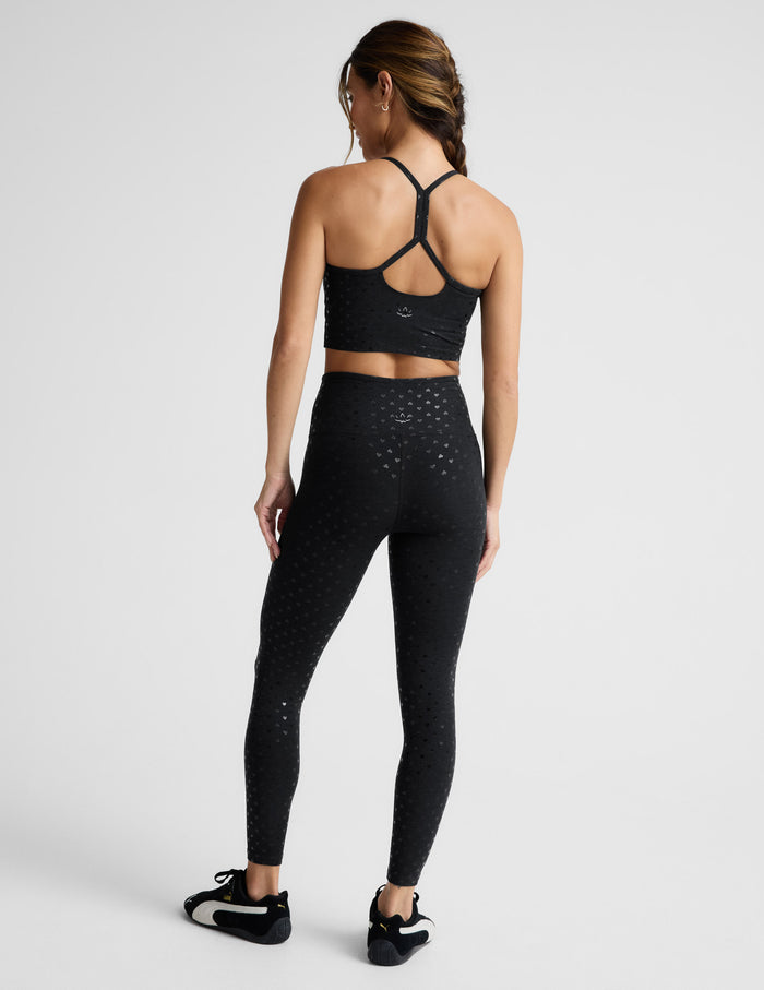 Woman wearing a black cropped tank with hearts print and leggings set on a light gray background.