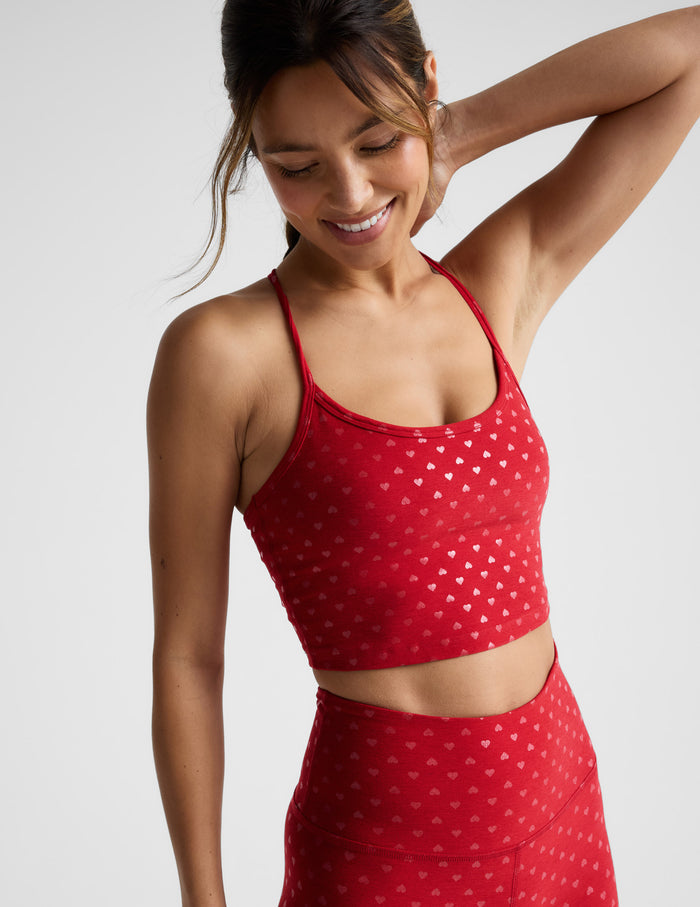 Woman wearing a red cropped tank with a hearts print and leggings with a plain background.