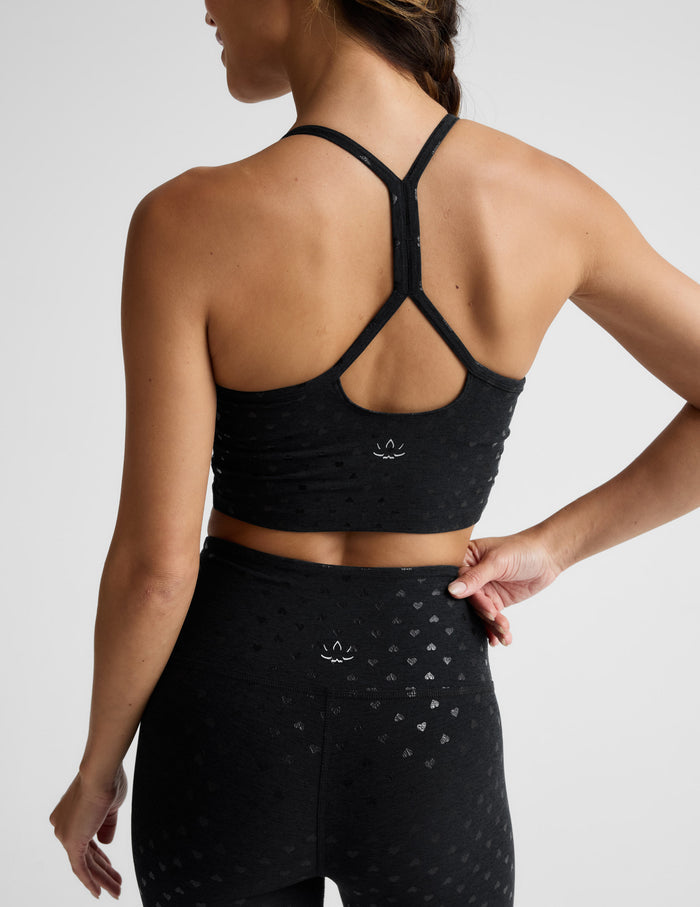 Woman wearing a black cropped tank with a hearts print and matching leggings against a plain background.