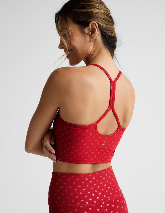 Woman wearing a red cropped tank with a hearts print and leggings with a plain background.