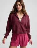 Woman wearing a burgundy zip-up sweatshirt and shorts against a plain background.