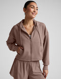 Woman wearing a brown full zip jacket and shorts against a plain background.