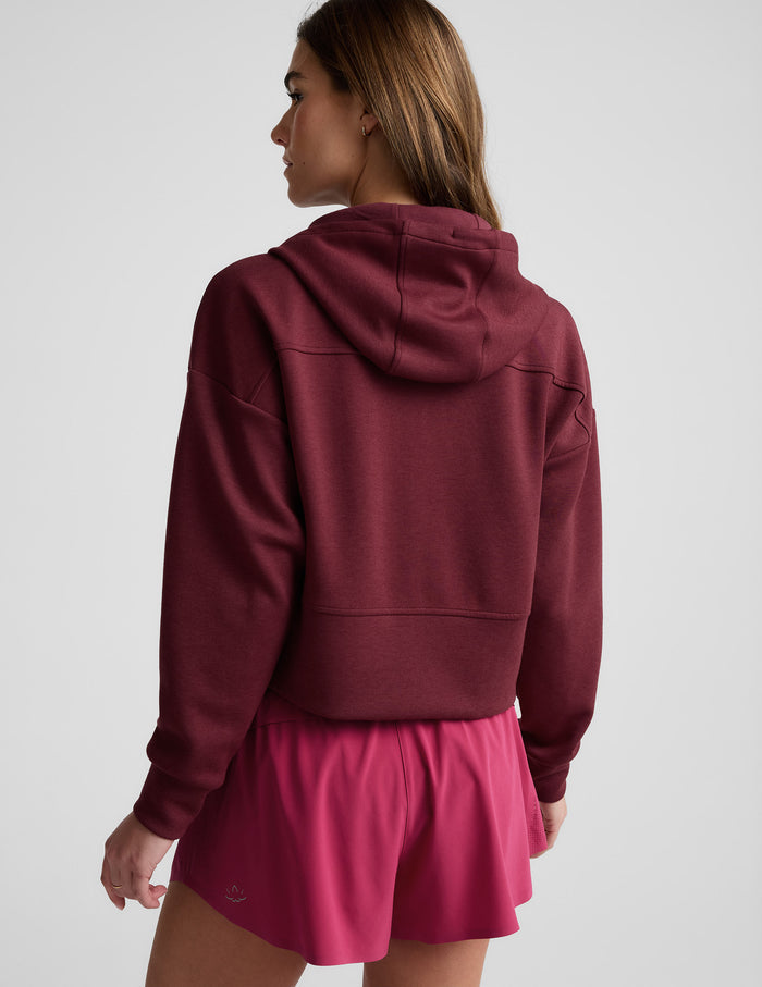 Woman wearing a burgundy zip-up sweatshirt and shorts against a plain background.