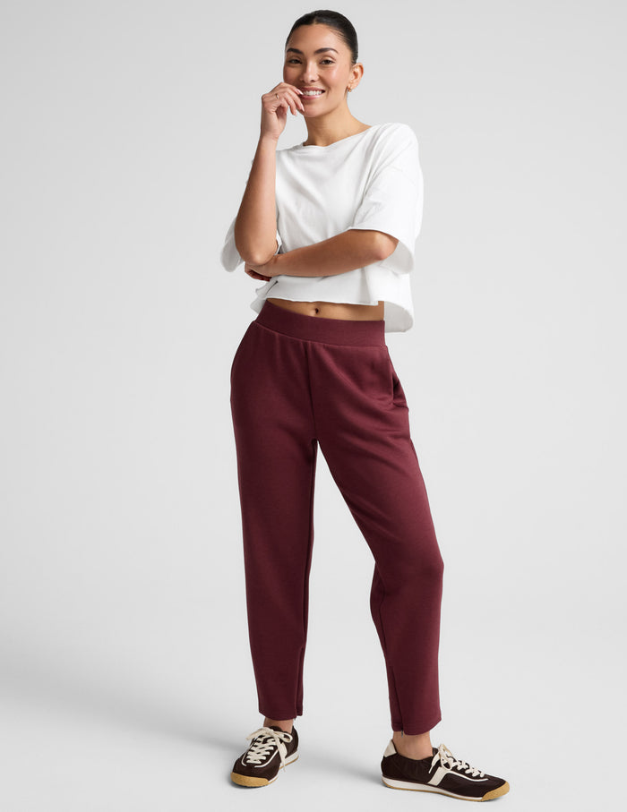 SoftSpring Tapered Pant in burgundy on a smiling model. Mid-rise, ankle-length tapered fit with a wide elastic waistband.