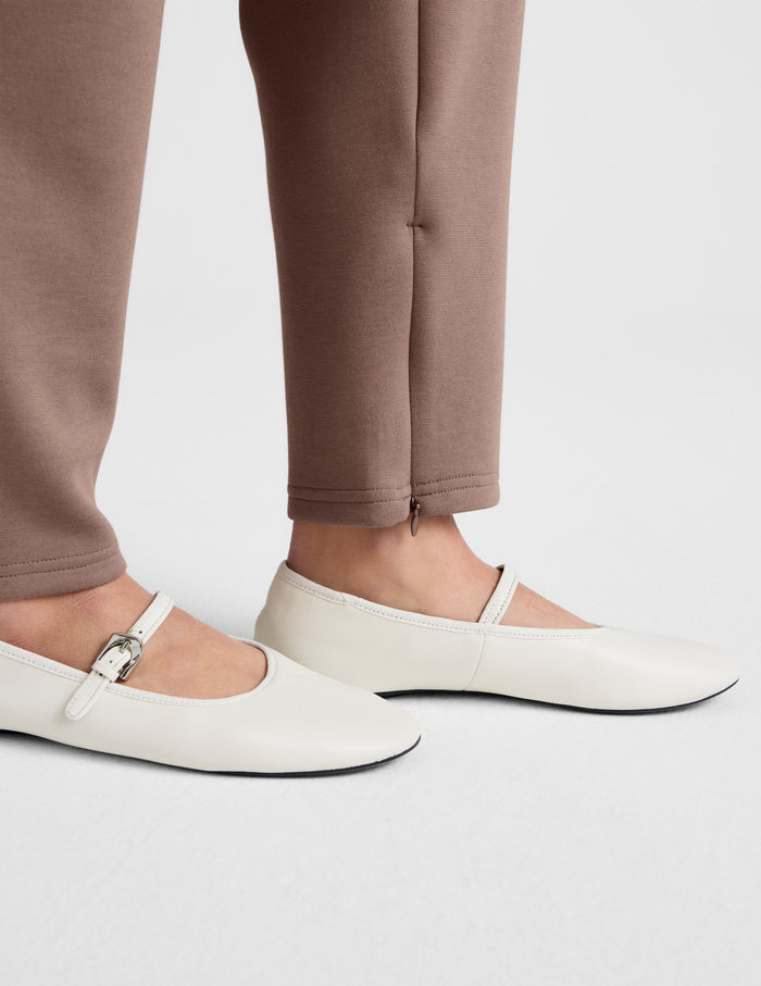 Low angle close-up of brown SoftSpring Tapered Pant featuring an ankle-length hem and styled with cream Mary Jane flats.