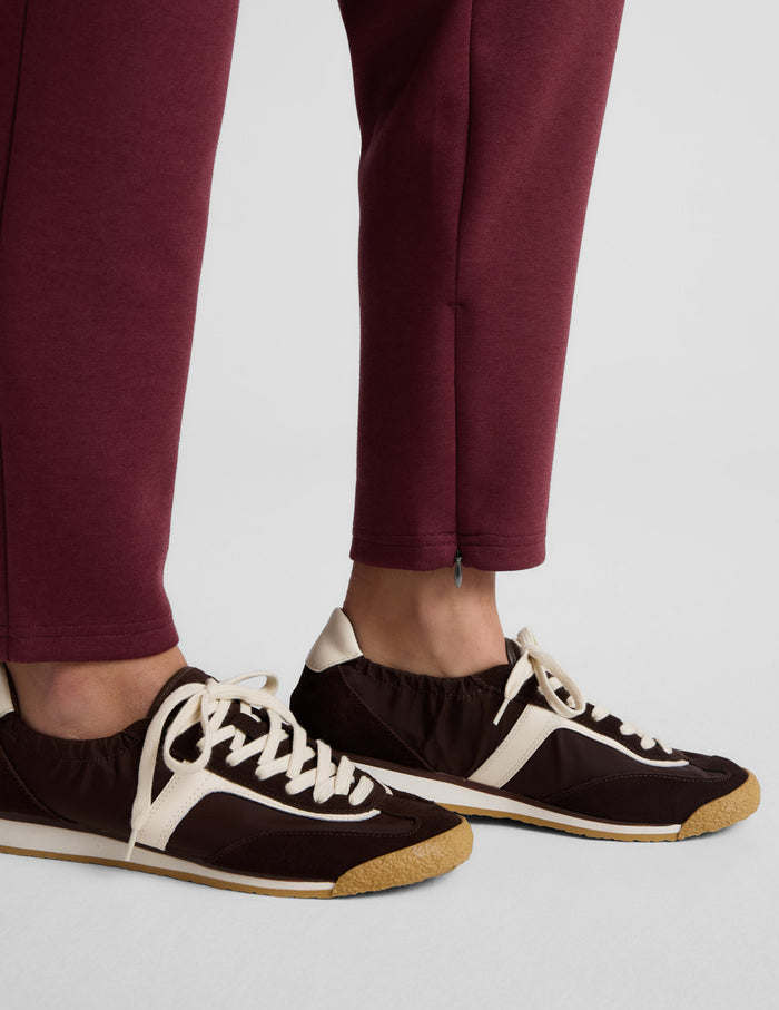 Burgundy SoftSpring Tapered Pant at ankle length with a small side zipper detail, styled with brown and cream sneakers.
