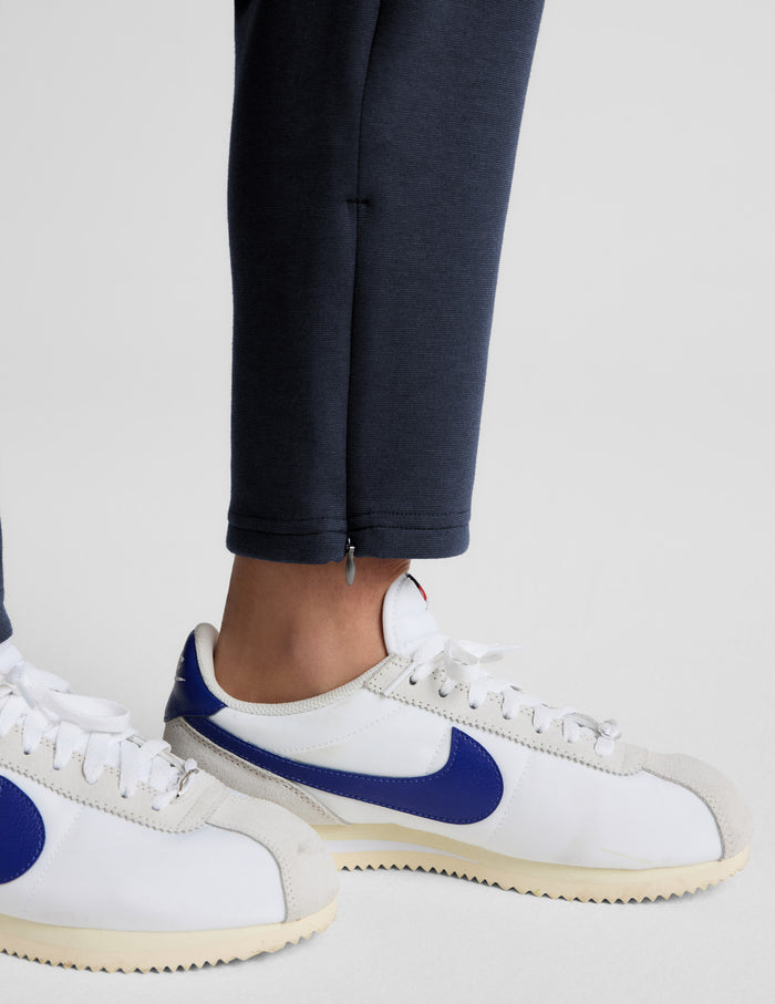 Close-up of the navy SoftSpring Tapered Pant ankle with side zipper detail, paired with white and blue sneakers.