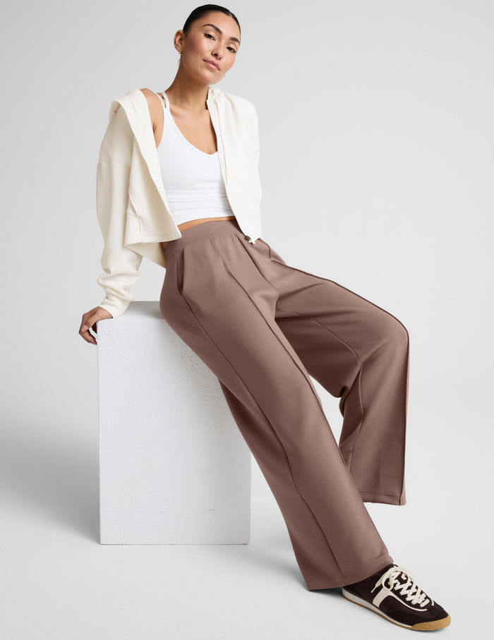 Woman wearing SoftSpring Wide Leg Pant in beige with front pintuck seams and a wide-leg silhouette, sitting on a white block.