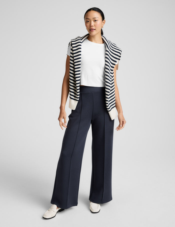 Black SoftSpring Wide Leg Pant with front pintuck seams, styled with a white tee and striped sweater on a standing model.