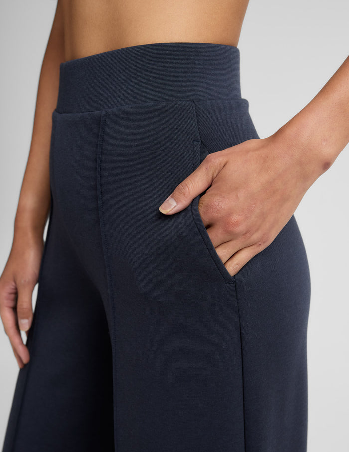 Close-up of black SoftSpring Wide Leg Pant showing the elastic waistband, slant pocket, and front pintuck fold detail.