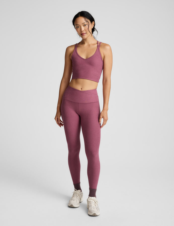 Woman wearing a matching mauve sports tank and leggings set on a light gray background.