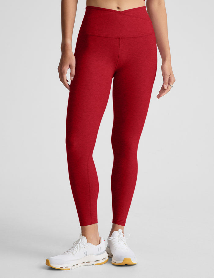 woman wearing red high-waisted midi length leggings with an overlapping waistband against a plain background.