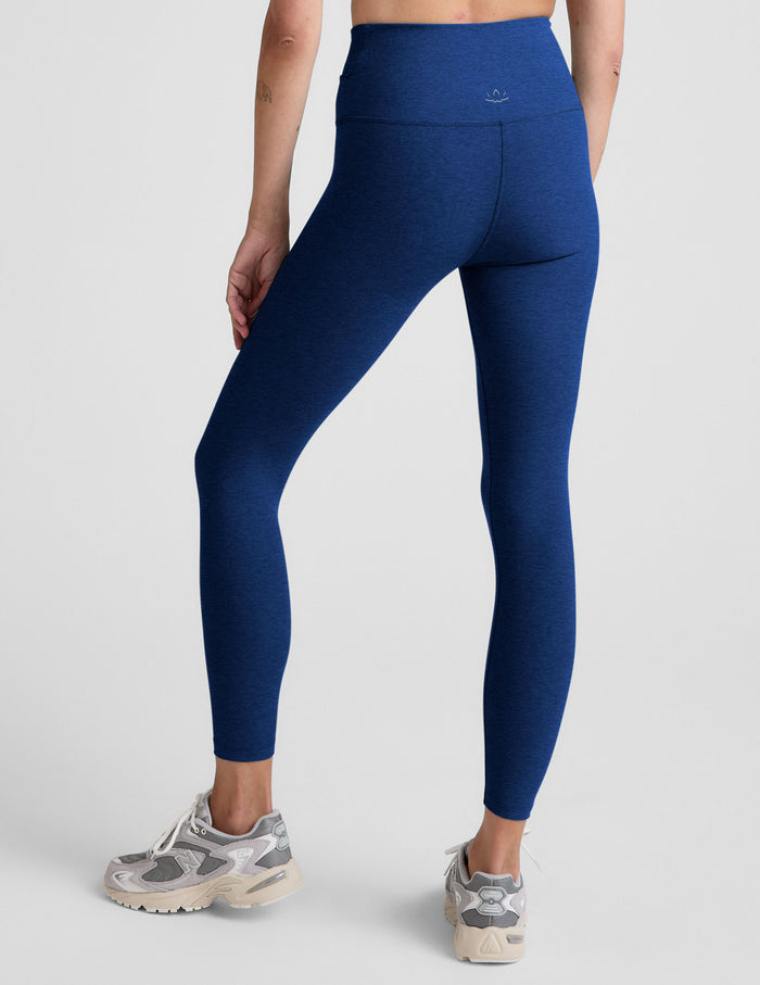 Woman wearing blue high-waisted midi leggings with a crossover front waistband against a plain background.