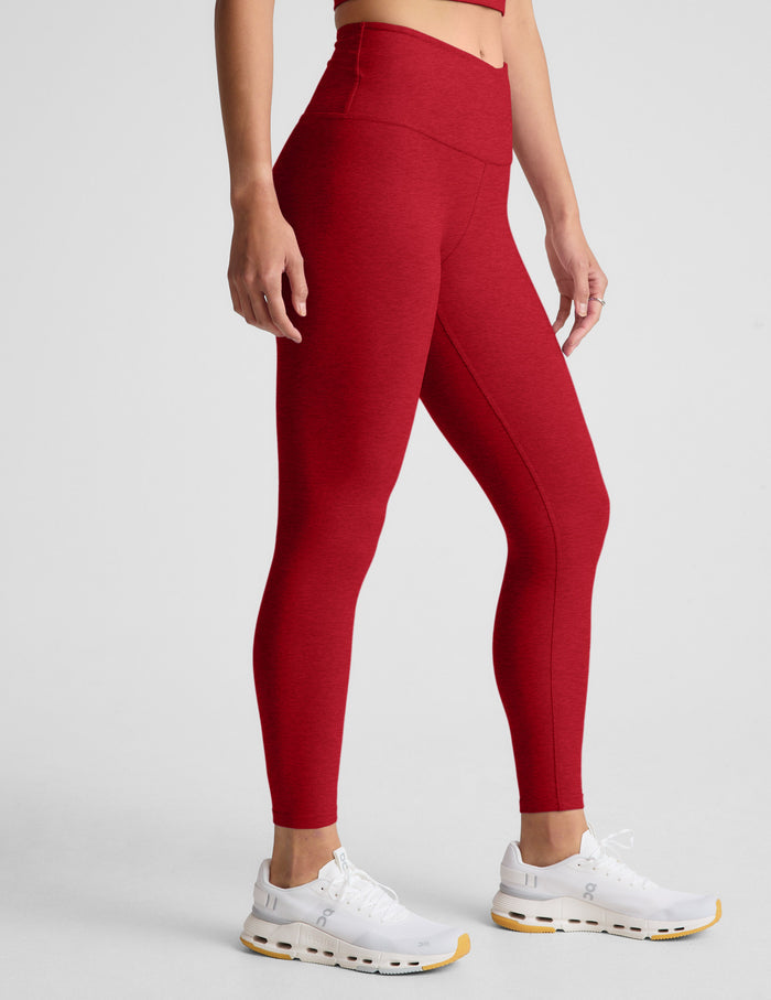 woman wearing red high-waisted midi length leggings with an overlapping waistband against a plain background.