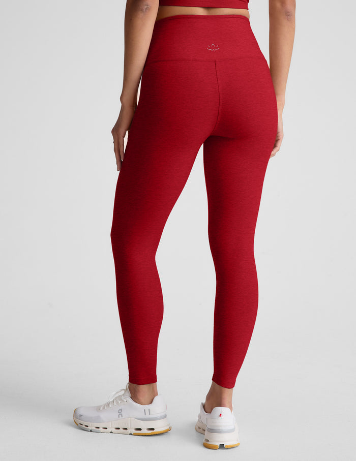 woman wearing red high-waisted midi length leggings with an overlapping waistband against a plain background.