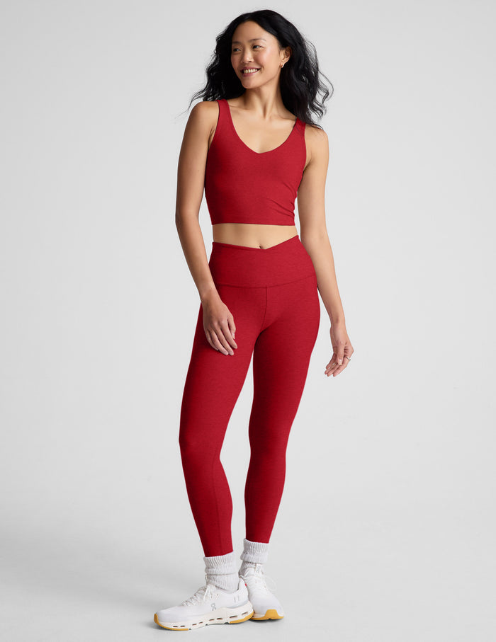 woman wearing red high-waisted midi length leggings with an overlapping waistband against a plain background.