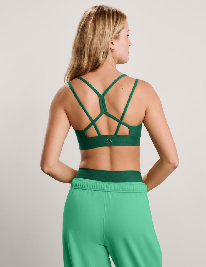 Woman wearing a green strappy bra and sweatpants against a plain background.
