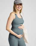 Pregnant woman wearing a gray tank top and cap on a light gray background.