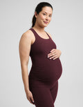 A pregnant woman wearing a matching dark burgundy maternity tank top and leggings set, standing against a solid light gray background.