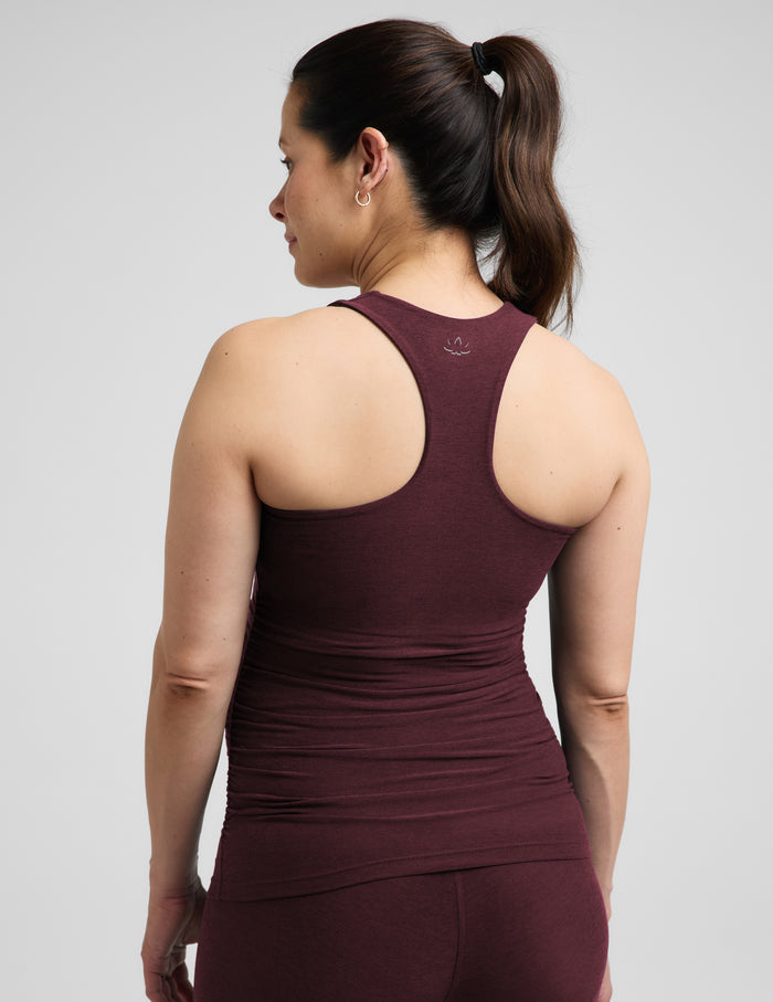 A pregnant woman wearing a matching dark burgundy maternity tank top and leggings set, standing against a solid light gray background.