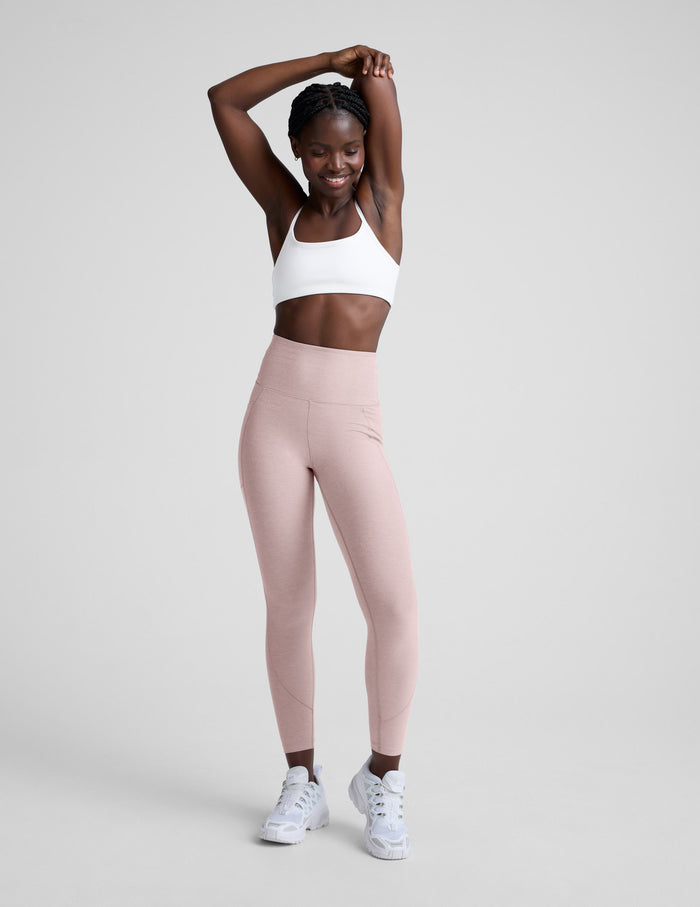 Woman wearing a white sports bra and pink leggings with pockets on a light gray background.