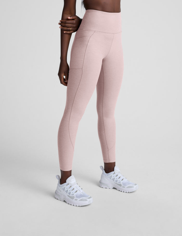 Person wearing light pink leggings with pockets and white sneakers on a plain background.
