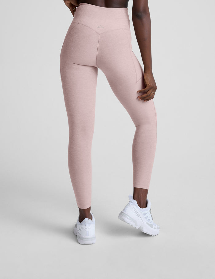 Person wearing light pink leggings with pockets and white sneakers on a plain background.