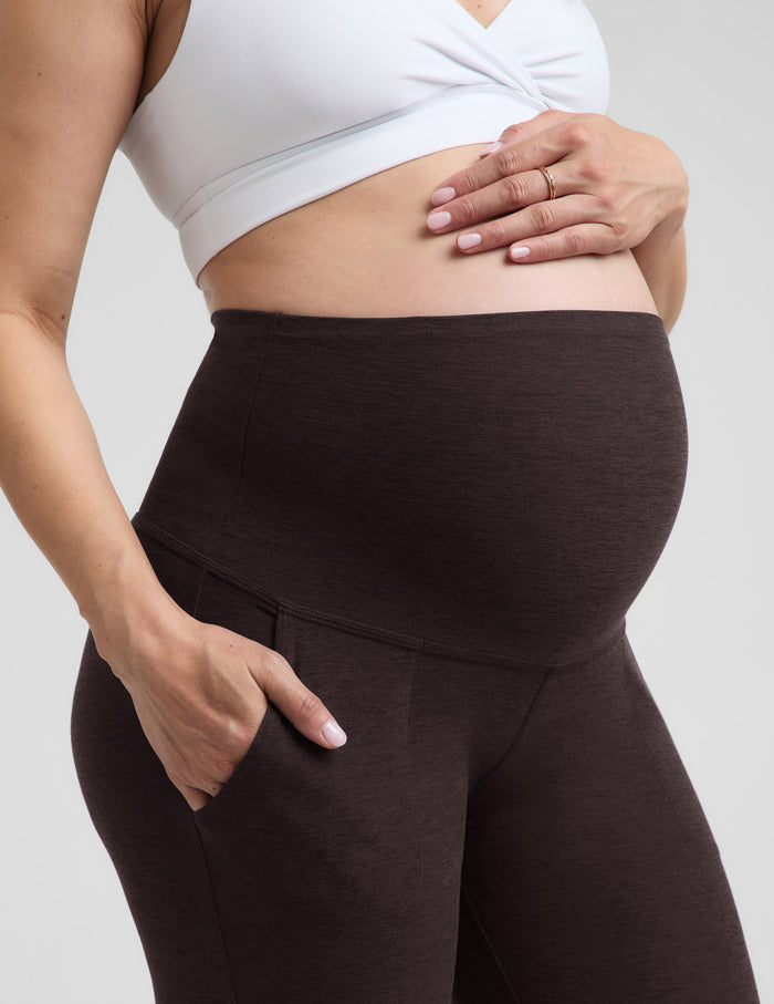 Woman wearing a white nursing bra and brown maternity joggers against a plain background.
