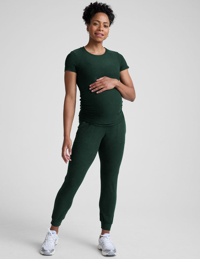 Pregnant woman in emerald Spacedye Beyond the Bump Maternity Midi Jogger, slim fit with cuffed ankles, hand on her belly.