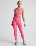 Woman wearing a pink bra and 7/8 length high waisted leggings against a plain background.