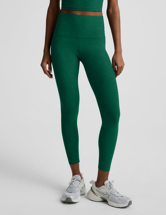 Woman wearing a green racerback cropped tank top and green high-waisted midi leggings against a plain background.