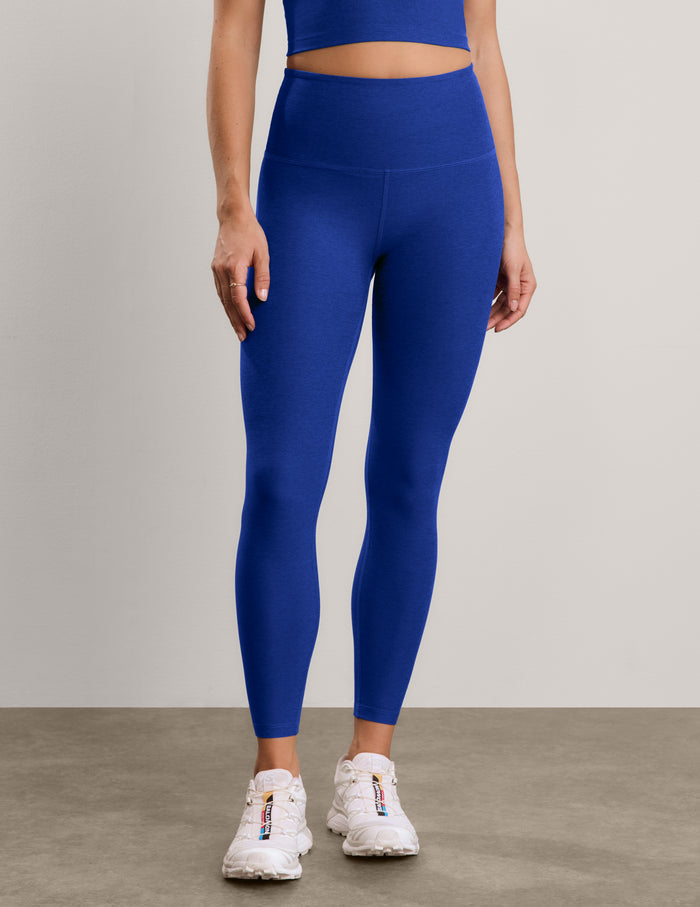 A woman modeling a matching royal blue activewear set consisting of a cropped tank and high-waisted leggings, paired with white sneakers, against a neutral studio backdrop.