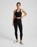 Woman wearing a black cropped tank and leggings on a light gray background.