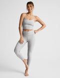 Woman wearing a gray tank and leggings on a white background.