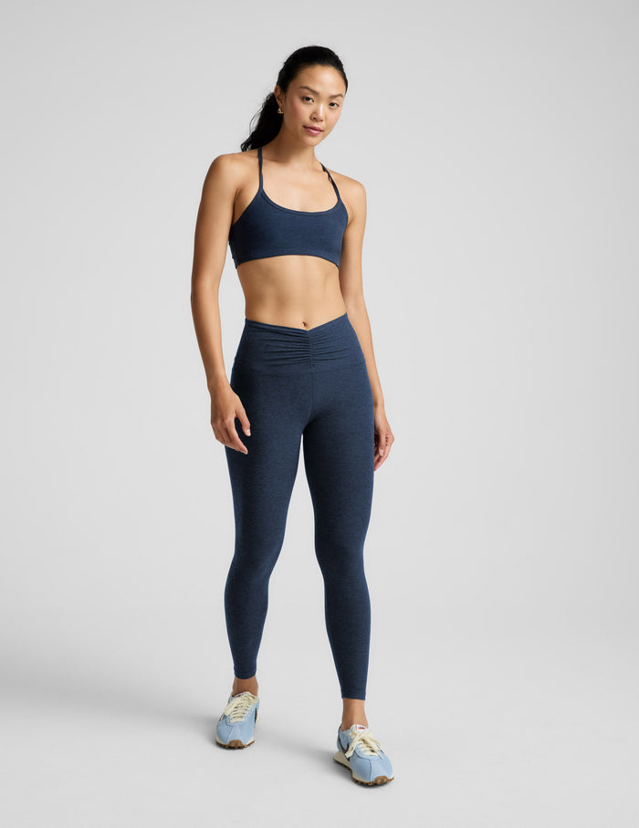 Woman wearing a navy sports bra and leggings set on a light gray background.