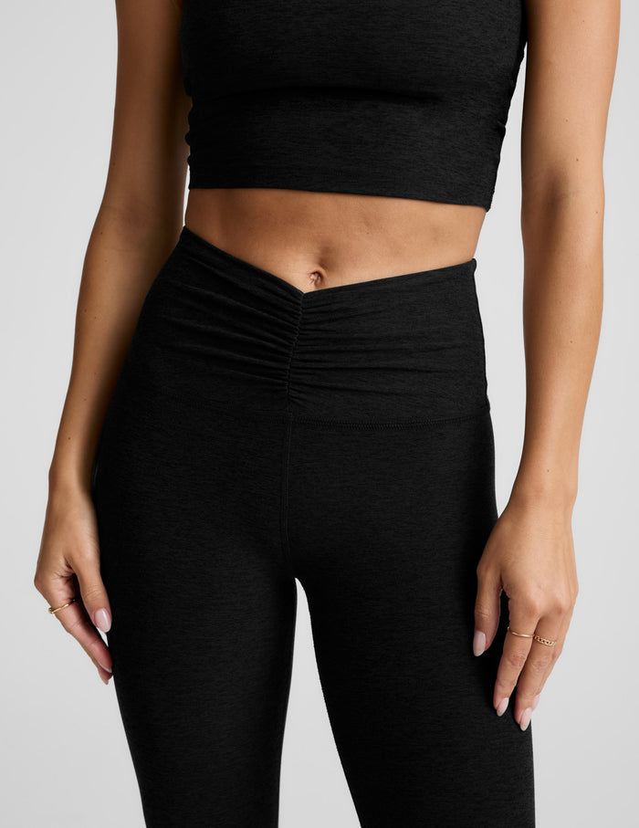 Person wearing black athletic leggings and crop top on a light gray background.