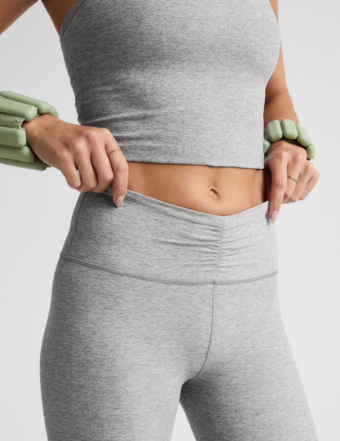 Person wearing gray athletic leggings and crop top on a light gray background.